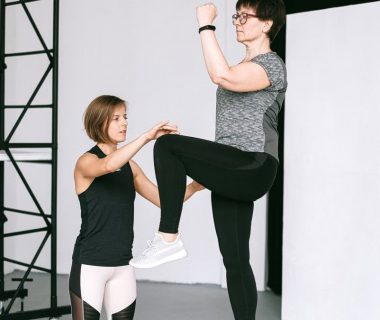 An elderly woman performs exercises with a fitness coach, focusing on a healthy lifestyle and wellness indoors.